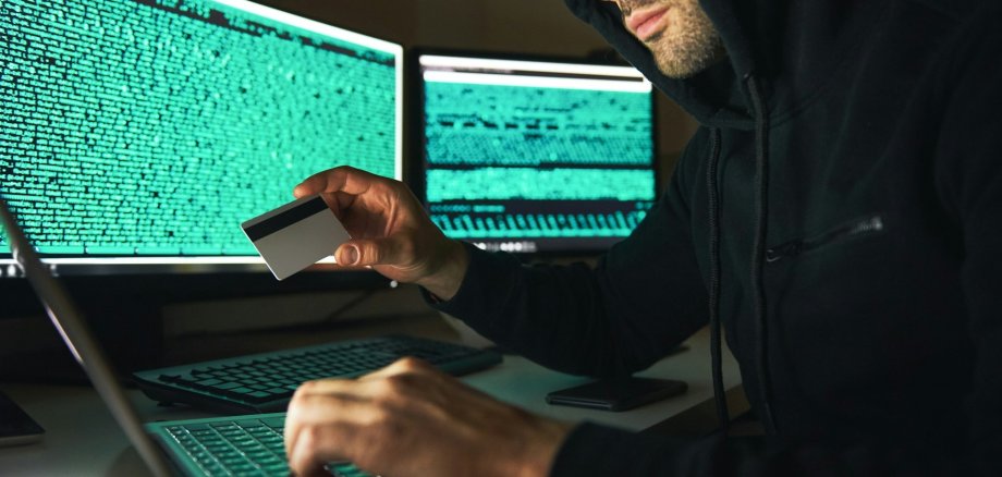 Cyberkriminalität Cyberkriminalität - ein Mann hält eine Kreditkarte und sitzt vor mehreren Monitoren