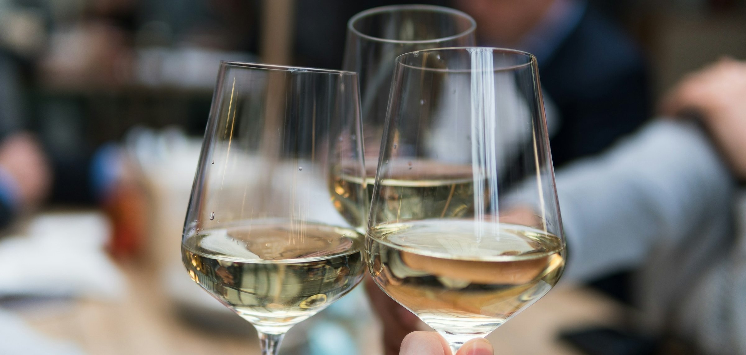 Drei Personen stoßen mit Weißwein an. Drei Personen stoßen mit Weißwein an.