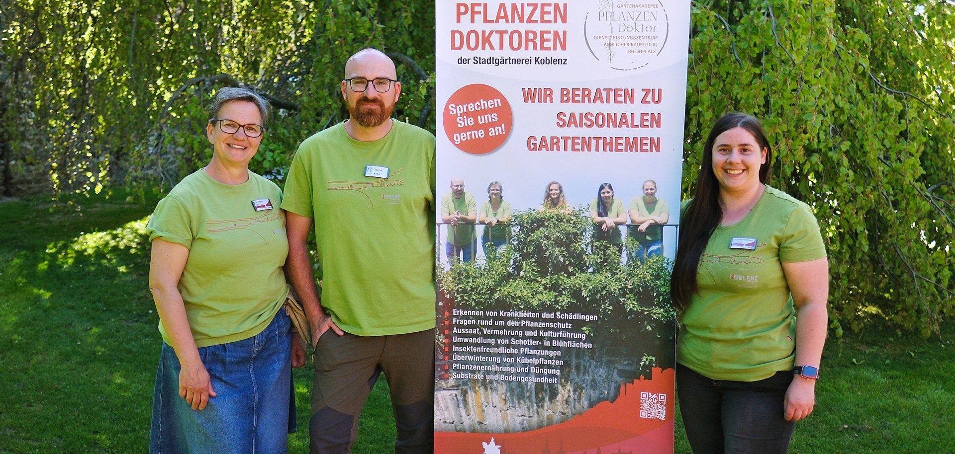 Zwei Frauen und ein Mann stehen vor einem Werbebanner.