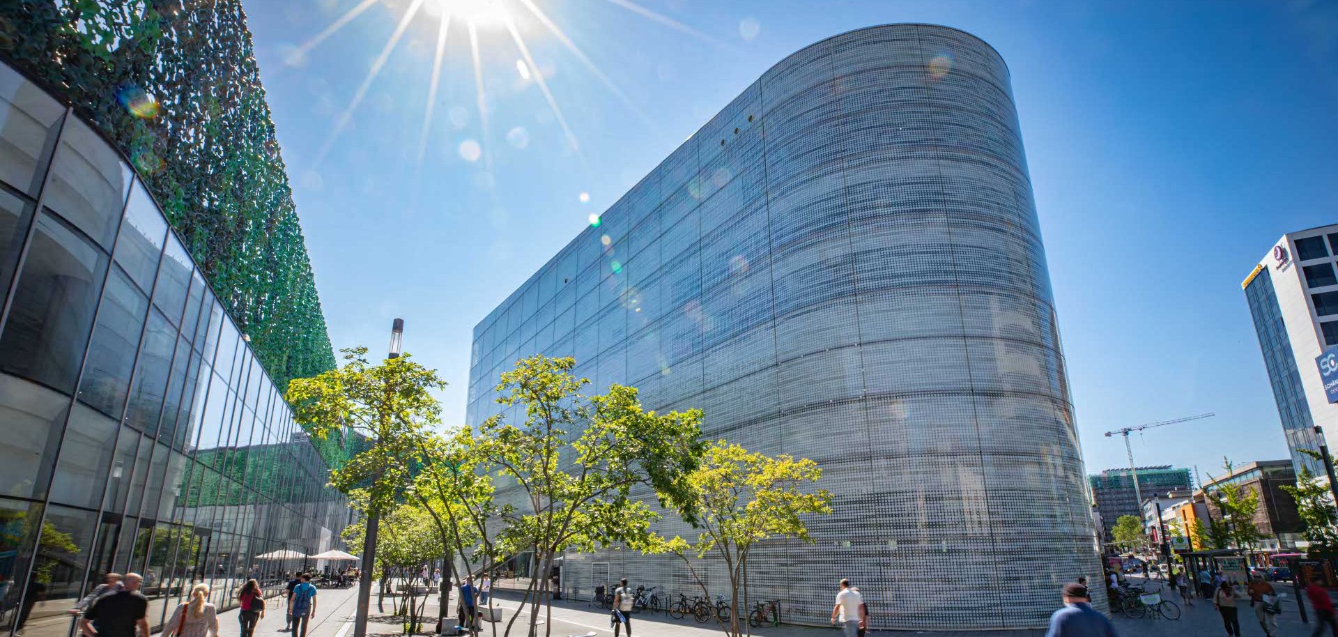 Ein Gebäude mit einer Glasfront steht auf einem belebten Platz.