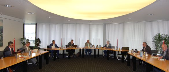 Vorstandssitzung Sportstiftung - acht Personen sitzen im Halbkreis an Tischen auf Abstand und durch Plexiglaswände getrennt.