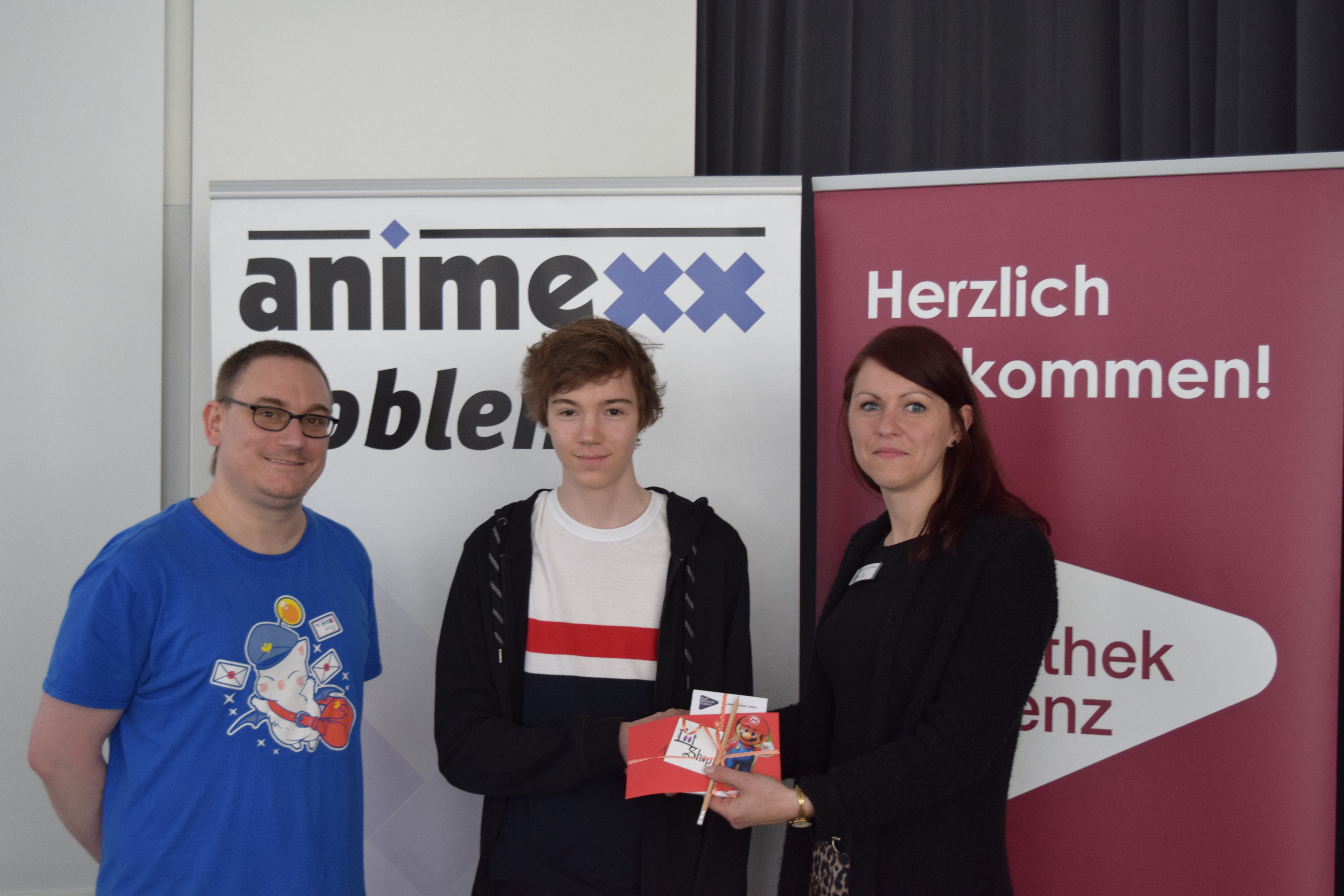 Lamy vom Koblenzer Loot Shop und Julia Löffler von der StadtBibliothek Koblenz übergeben dem Gewinner des Mario Kart - Turnier den Preis 