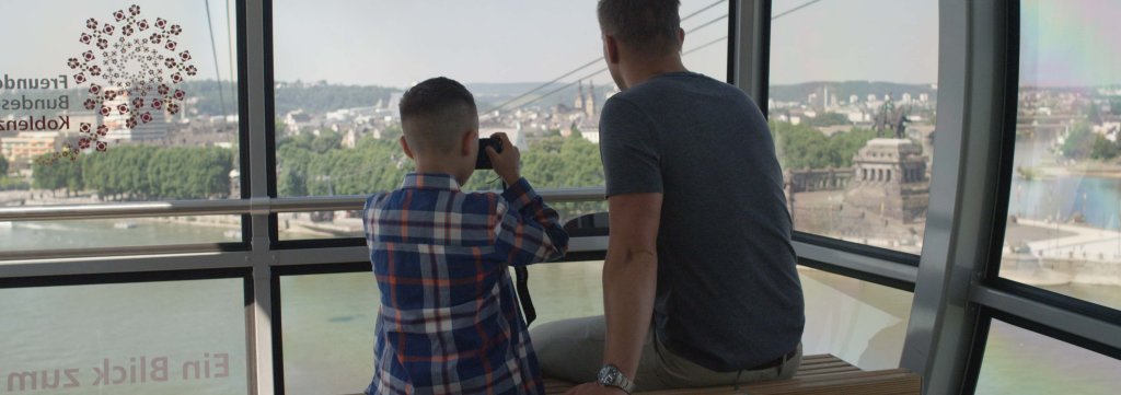 Vater und Sohn in der Seilbahn sitzend mit Blick auf Altstadt und Deutsches Eck