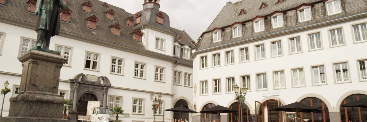 Jesuitenplatz mit zwei weißen Gebäuden, Platzfläche und Denkmal darauf