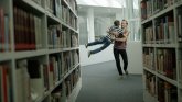 Ein Mann schwenkt im Spiel einen Jungen zwischen Bücherregalen einer Bibliothek.
