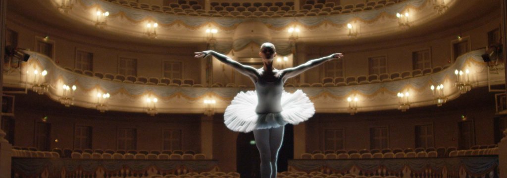 Eine Ballerina tanzt vor der beleuchteten aber menschenleeren Kulisse des Theaters Koblenz. 
