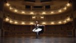 Eine Ballerina tanzt vor der beleuchteten aber menschenleeren Kulisse des Theaters Koblenz. 