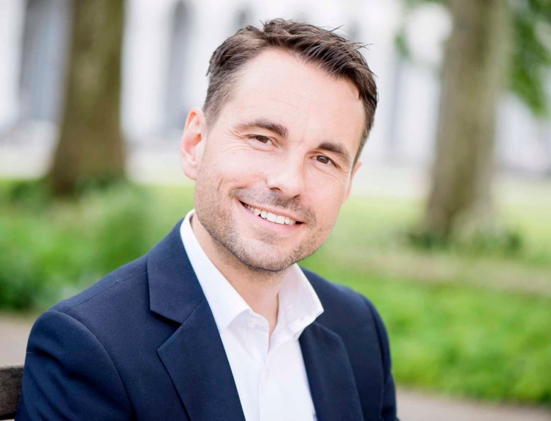 Oberbürgermeister David Langner Oberbürgermeister David Langner Portrait, blaues Sakko, weißes Hemd, im Hintergrund zwei Bäume
