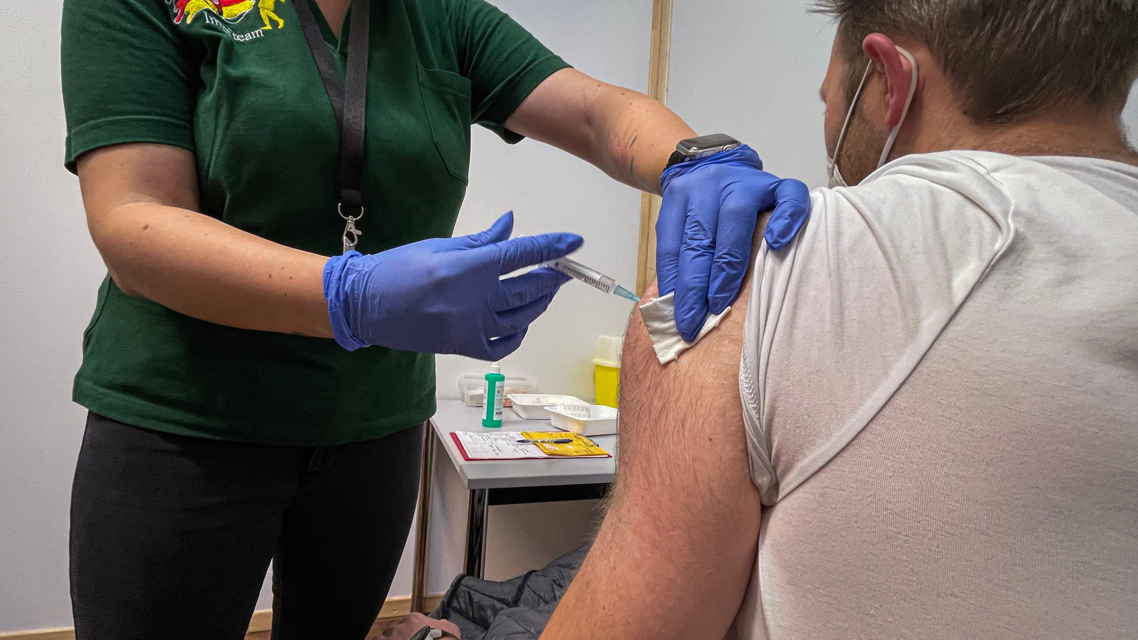 Ein Mann wird geimpft - sichtbar: Eine Frau spritzt Impfstoff in den linken Oberarm eines Mannes.