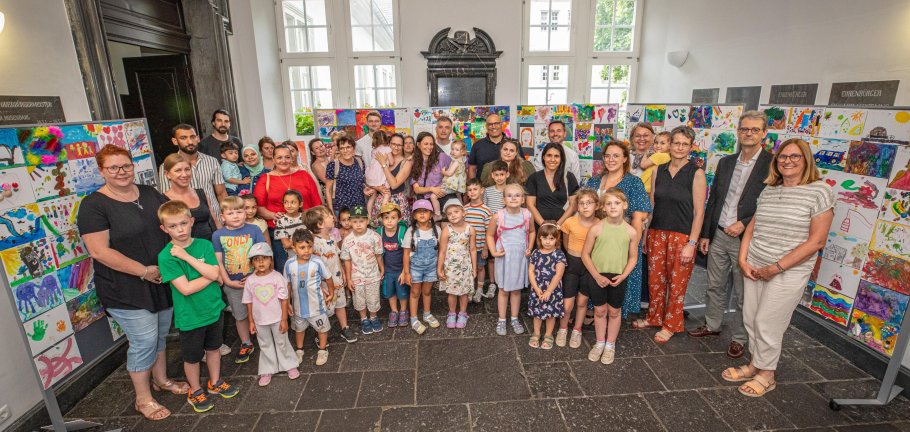 Eine Gruppe von Kindern und Erwachsenen die vor Stellwänden mit Bildern stehen.