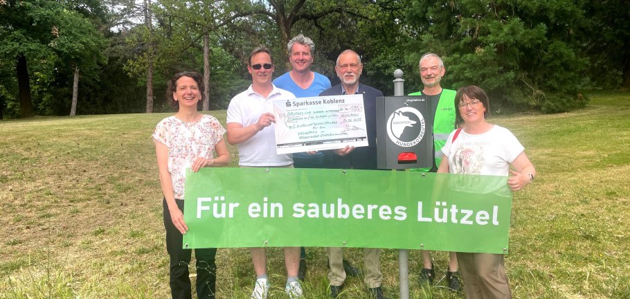 6 Personen stehen um einen Hundekotbeutelspender. Zwei halten ein Banner und 2 einen großen Scheck.