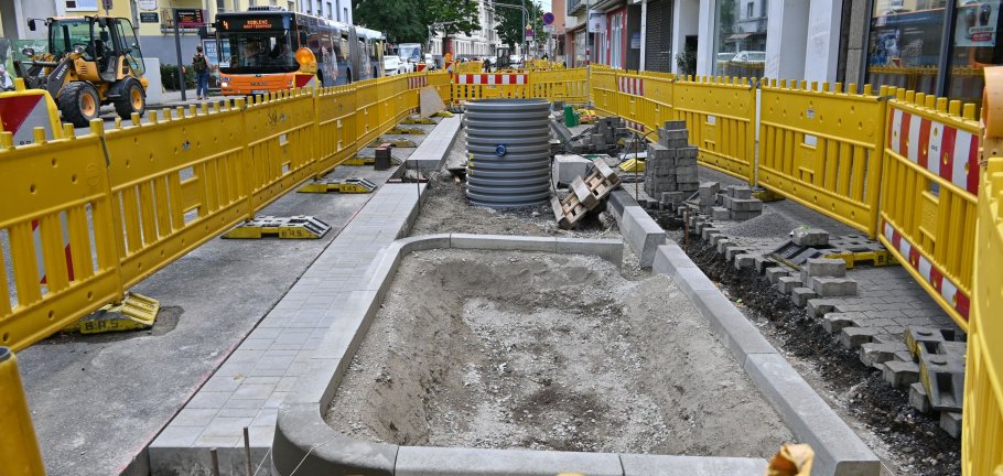 Blick über einen Bauzaun. Ein künftiges Baumbeet im Vordergrund. Dahinter ein Wassertank, der noch eingbaut wird.