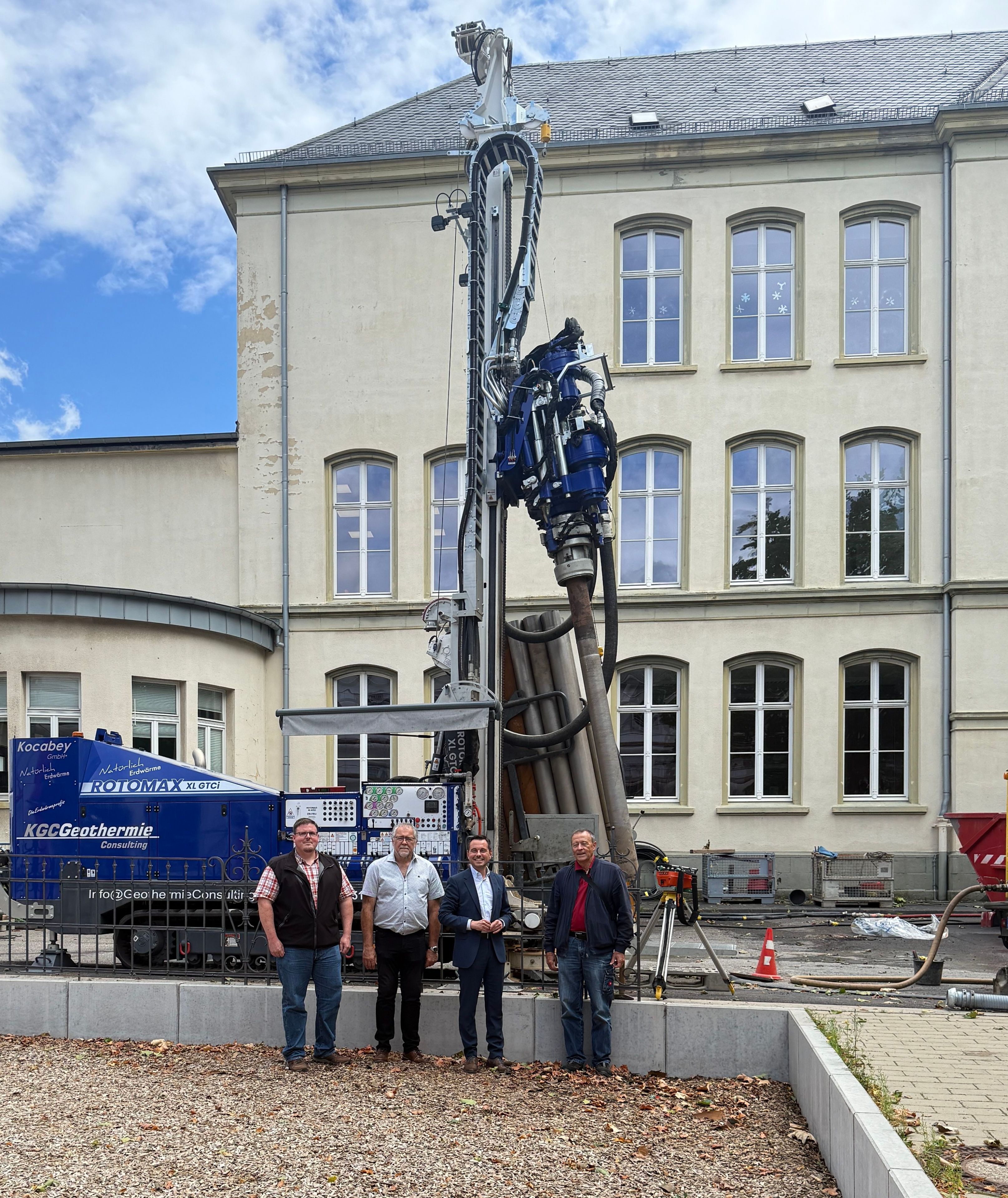 4 Männer stehen vor einem großen Erdbohrgerät auf einer Baustelle.