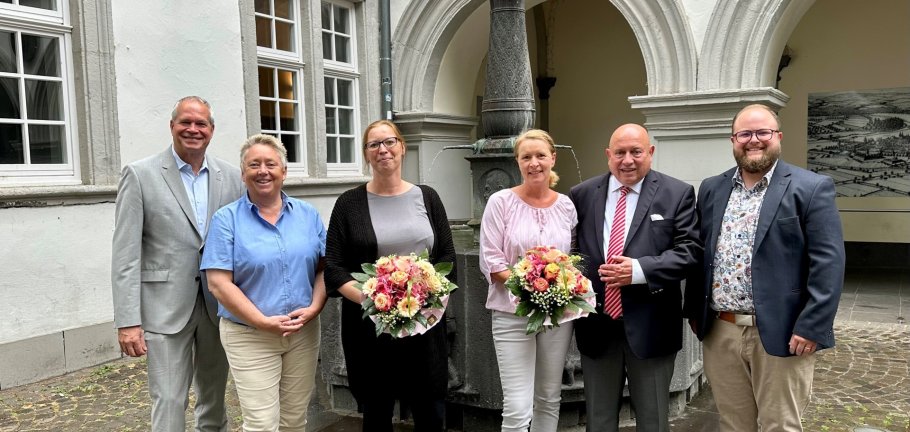 6 Personen, zwei davon mit Blumensträußen, stehen vor dem Schängelbrunnen.