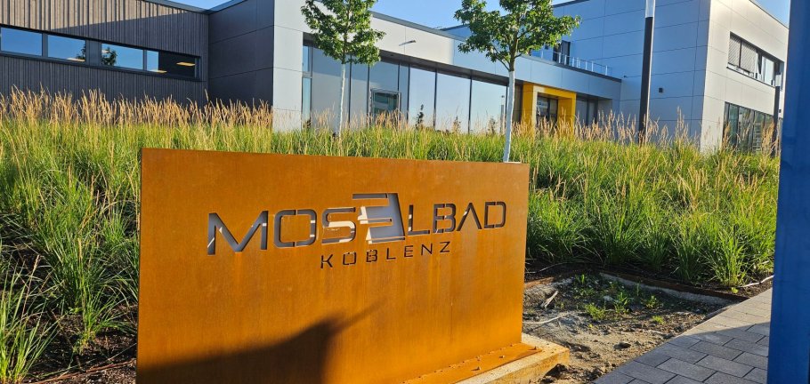 Die Außenansicht eines Hallenbades. Im Vordergrund ein Schild mit dem Namenszug des Bades.