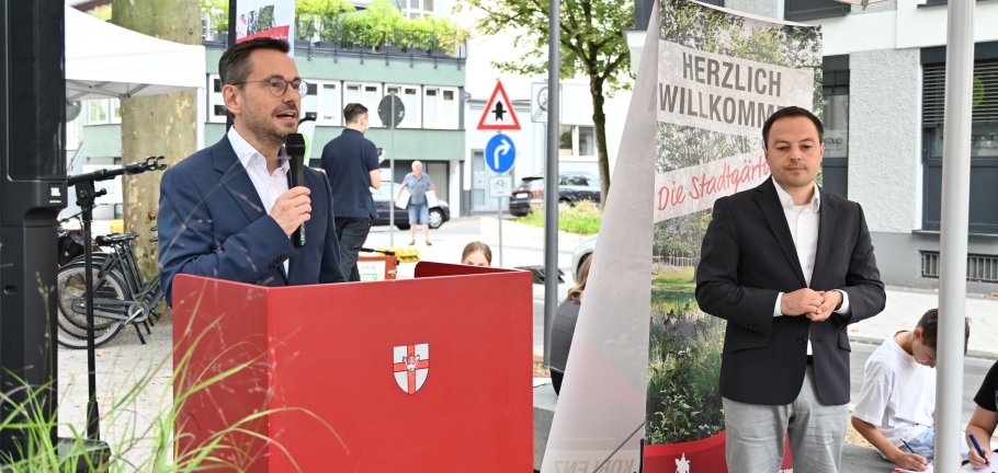 2 Männer stehen unter einem Zeltdach, einer hat ein Mikrophon in der Hand.