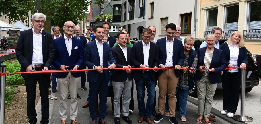 Viele Menschen hinter einem roten Band, einige zerschneiden es mit Scheren.