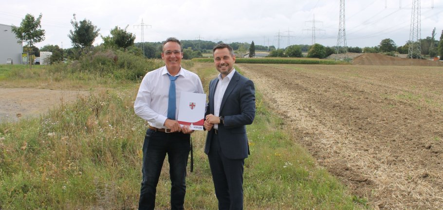 2 Männer stehen an einem Endstück eines Weges. Im Hintergrund Felder.