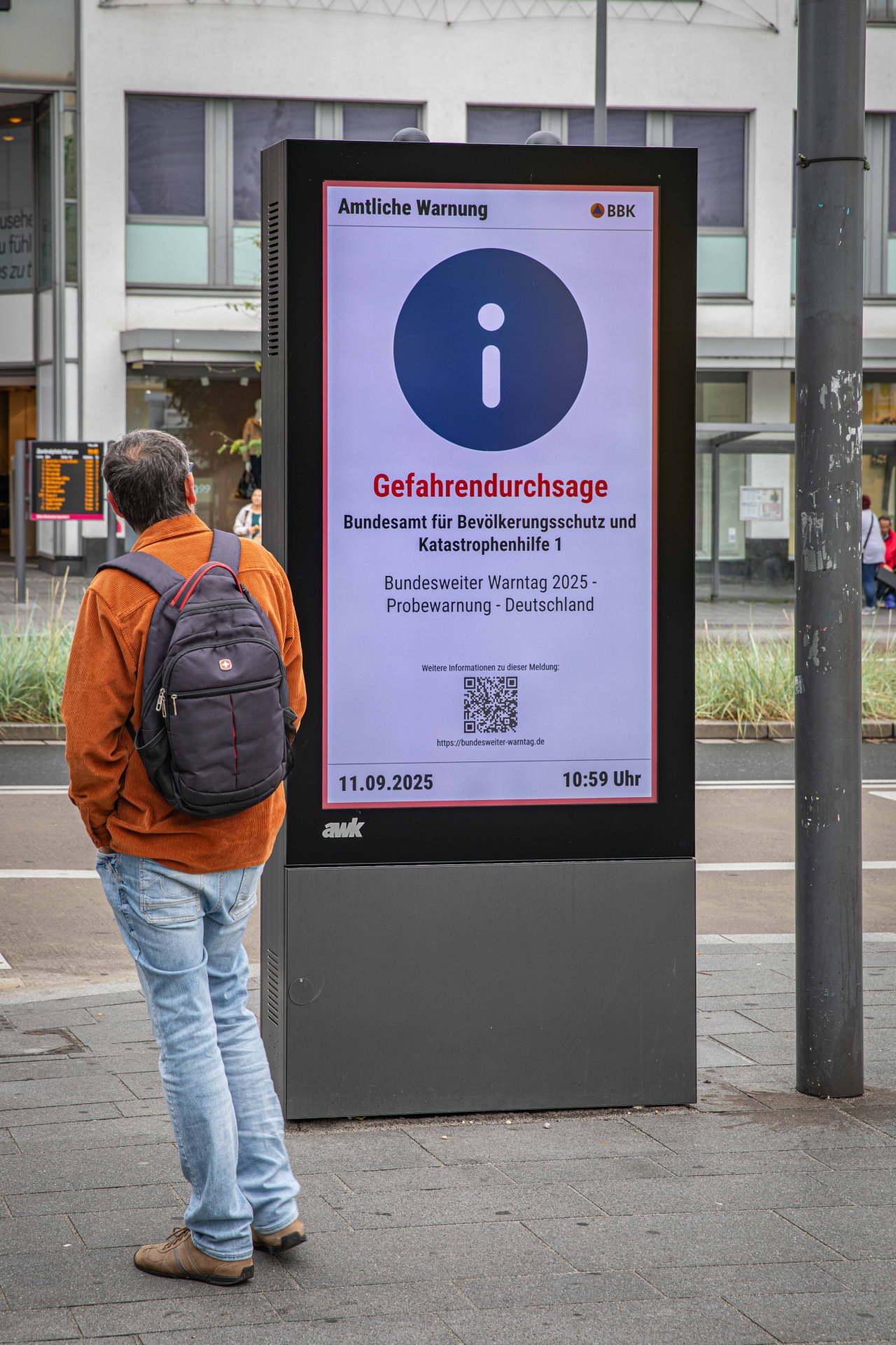 Ein Mann steht vor einer digitalen Anzeigetafel und liest die Warnung darauf.