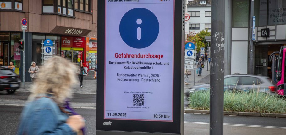 Ein Frau läuft an einer digitalen Anzeigetafel vorbei und liest die Warnung darauf.