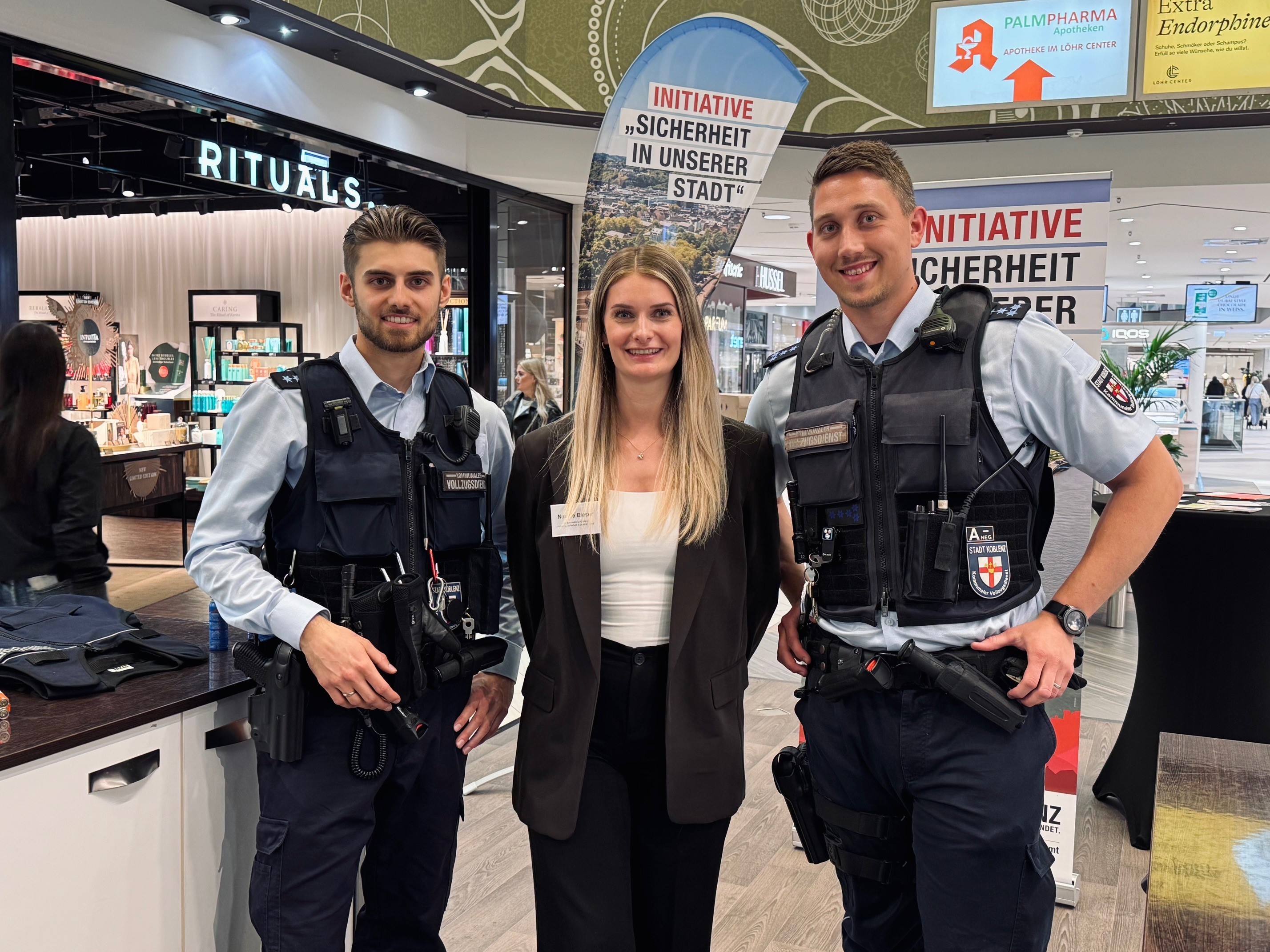 Eine Frau flankiert von 2 uniformierten Männern.