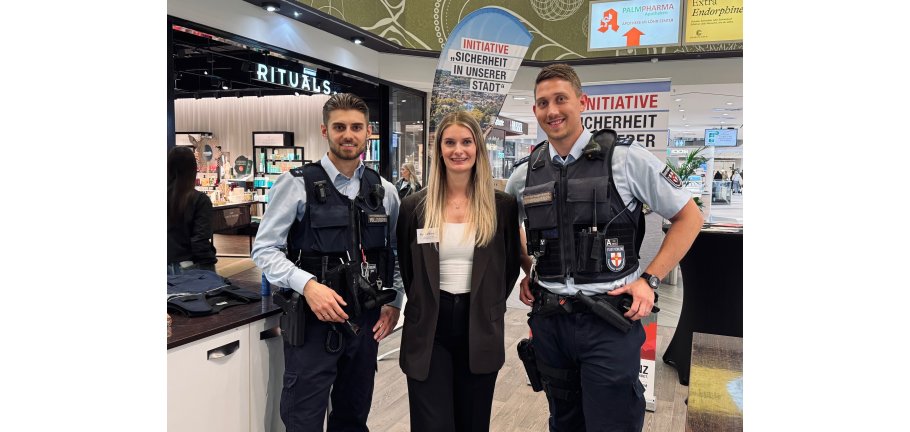 Eine Frau flankiert von 2 uniformierten Männern.