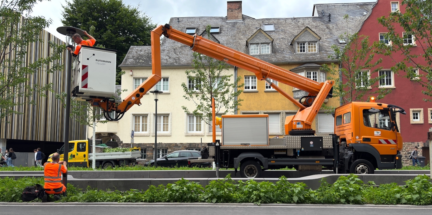 Ein Mann im Korb eines Hubsteigers wechselt ein Leuchtmittel einer Straßenlaterne.