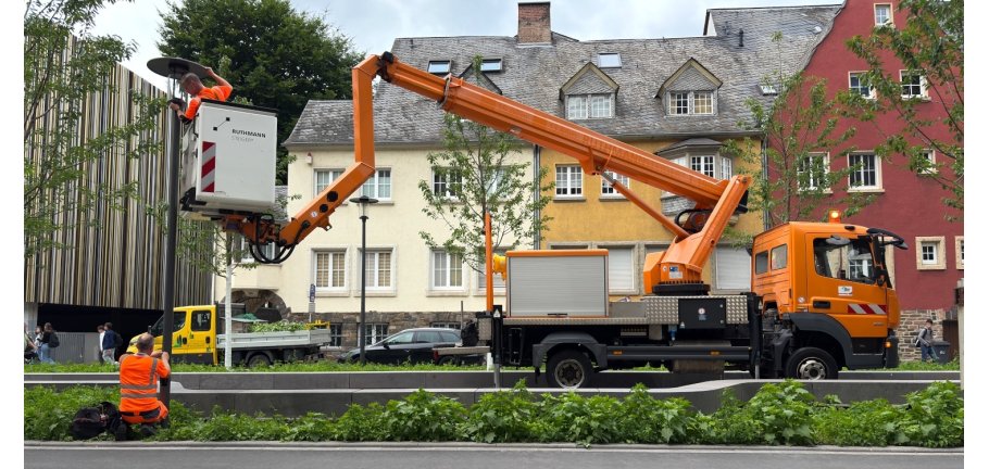Ein Mann im Korb eines Hubsteigers wechselt ein Leuchtmittel einer Straßenlaterne.