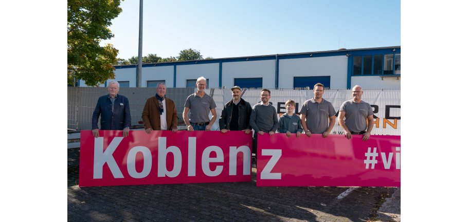 Viele Personen stehen hinter einem neue Werbeschild mit der Aufschrift Koblenz.