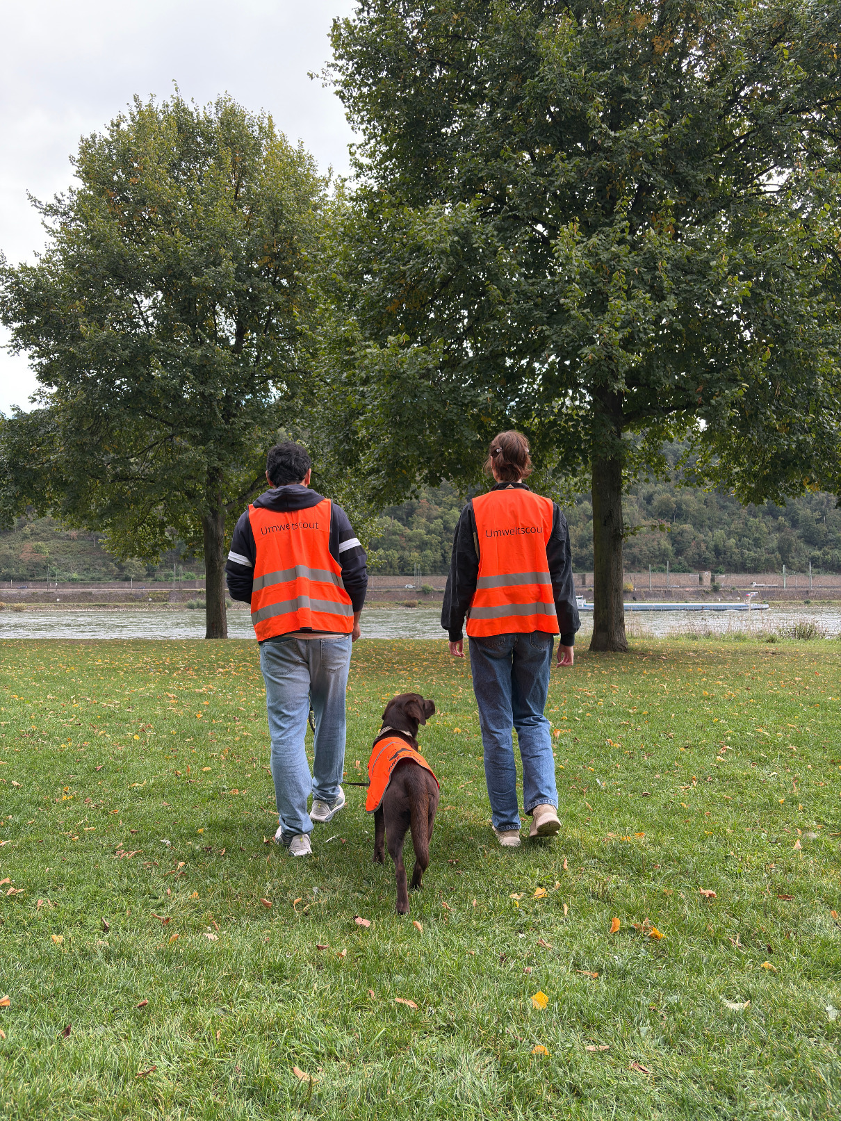 Zwei Umweltscouts samt ihrem Hund zu Fuß unterwegs am Rheinufer in Koblenz.