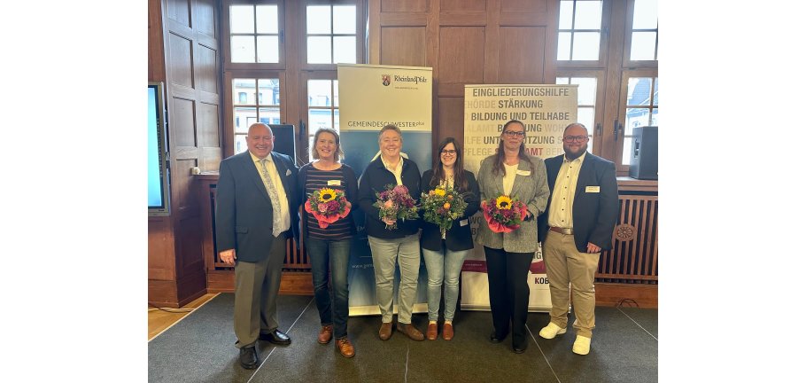 Vier Frauen mit Blumensträußen und zwei Männer stehen vor Roll-ups.