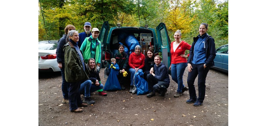 Eine größere Gruppe von Menschen steht bei einem Auto, dessen geöffneter Laderaum mit vielen Müllsäcken gefüllt ist.