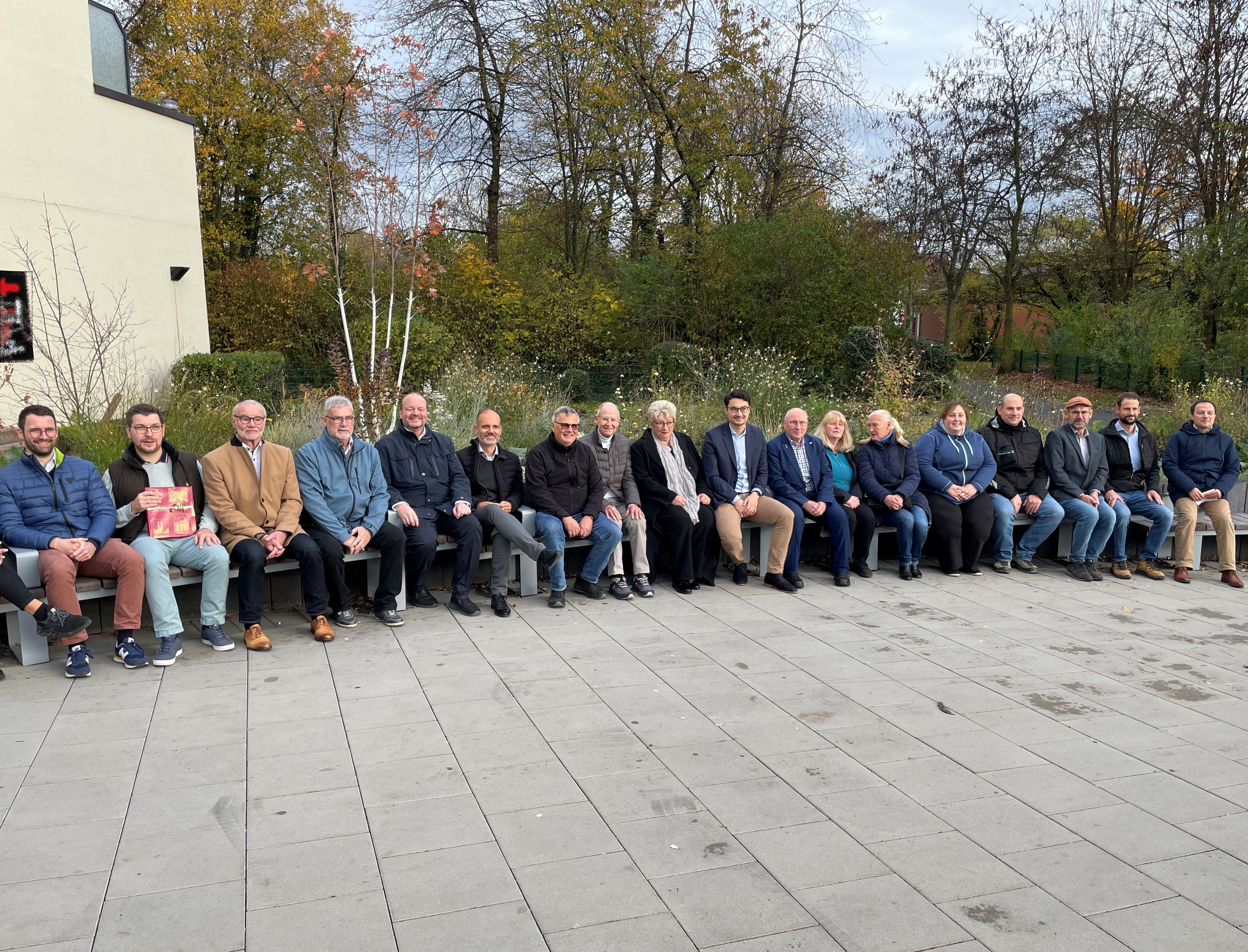 Viele Menschen sitzen auf einer langen Sitzbank.