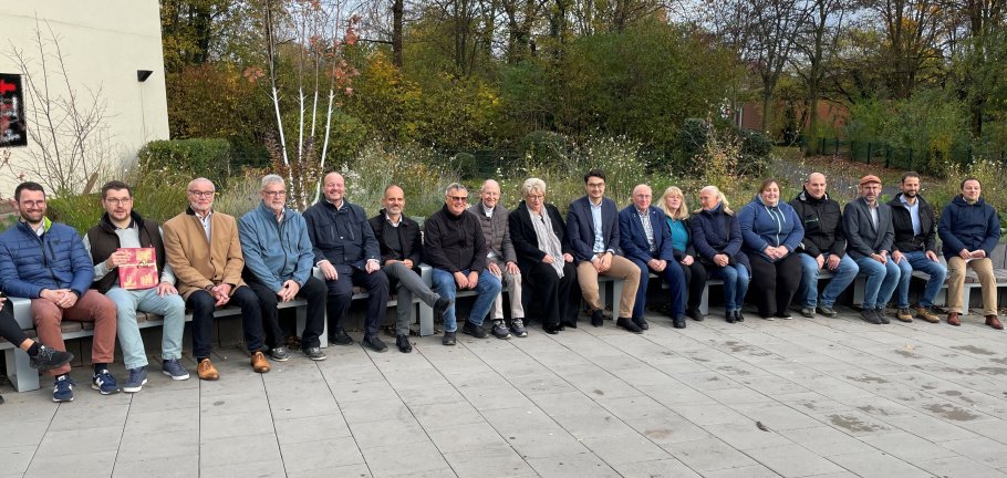 Viele Menschen sitzen auf einer langen Sitzbank.