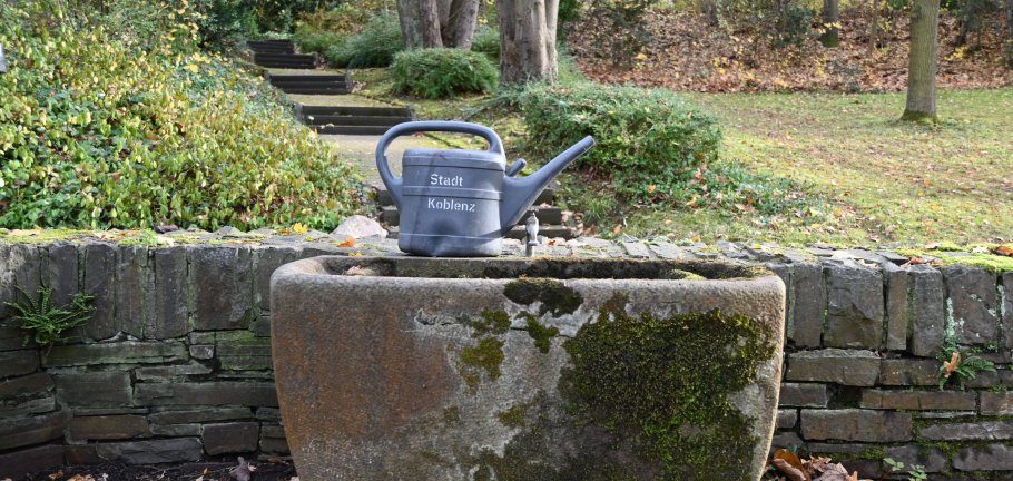Eine Gießkanne auf einem Brunnenrand.