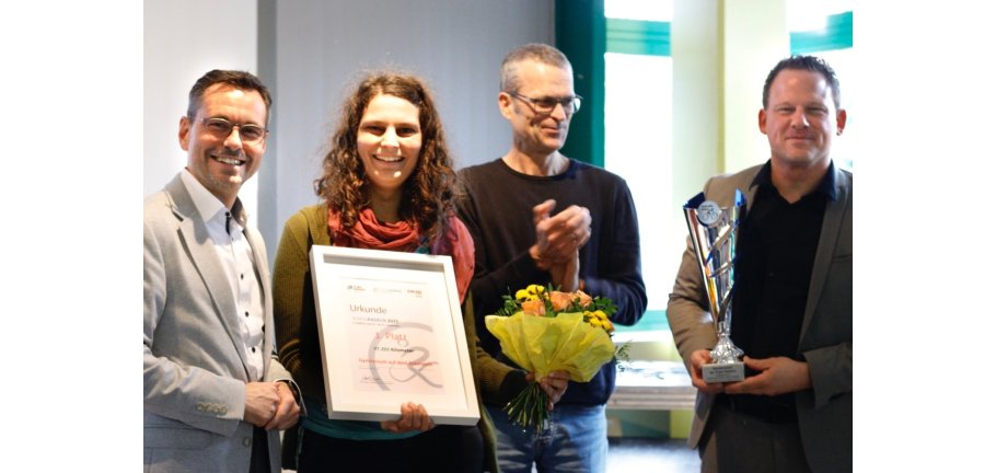 4 Personen mit Urkunde, Pokal und Blumenstrauß bei einer Preisverleihung.