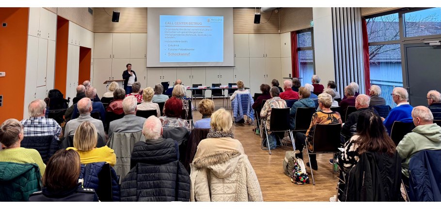 Viele Menschen in einem Saal. Vorne steht eine Rednerin.