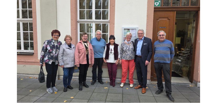 Vor einer Hauswand stehen eine Reihe von Menschen und Blicken in die Kamera.