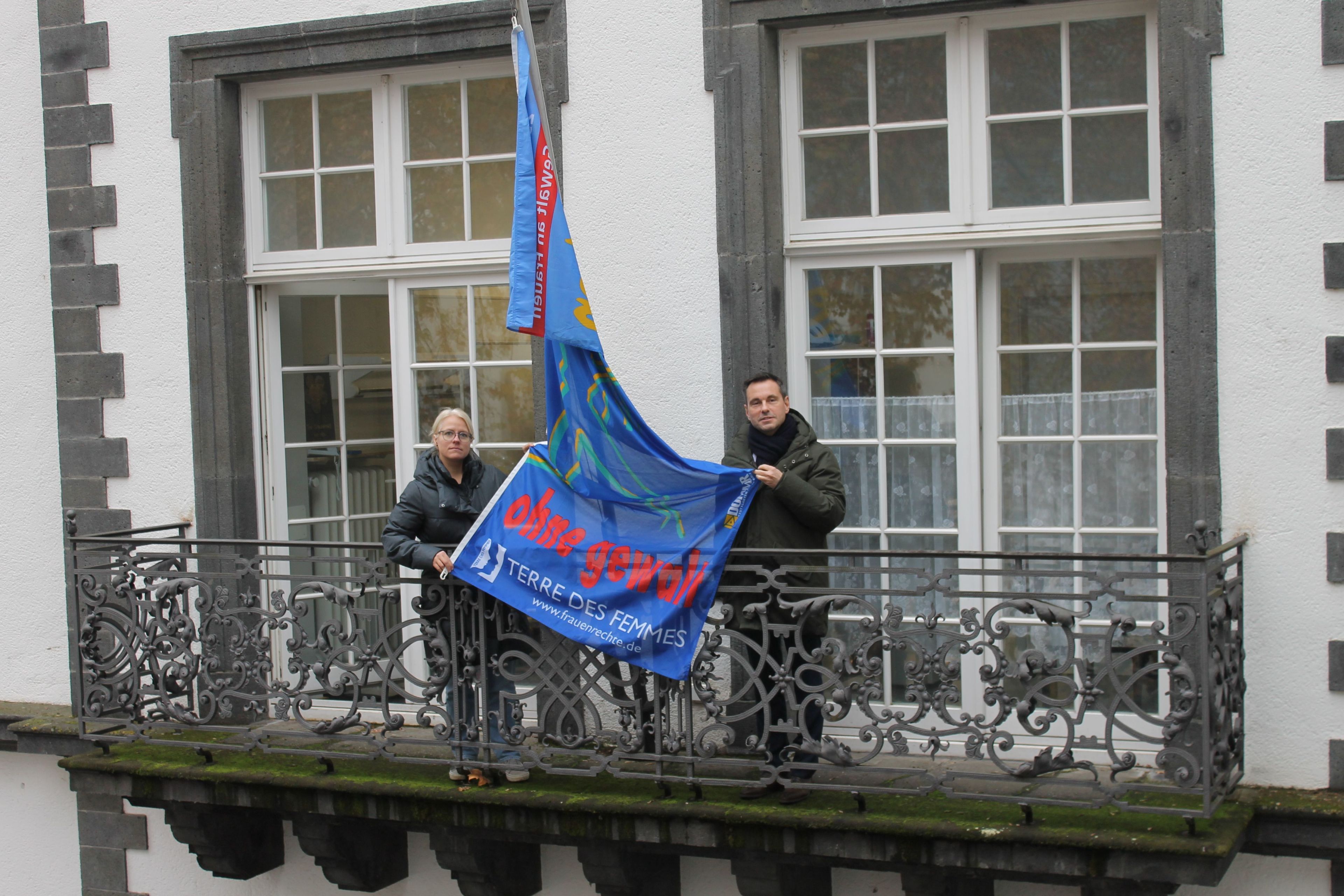 Ein Mann und eine Frau auf einem Balkon zwischen ihnen eine Fahne.