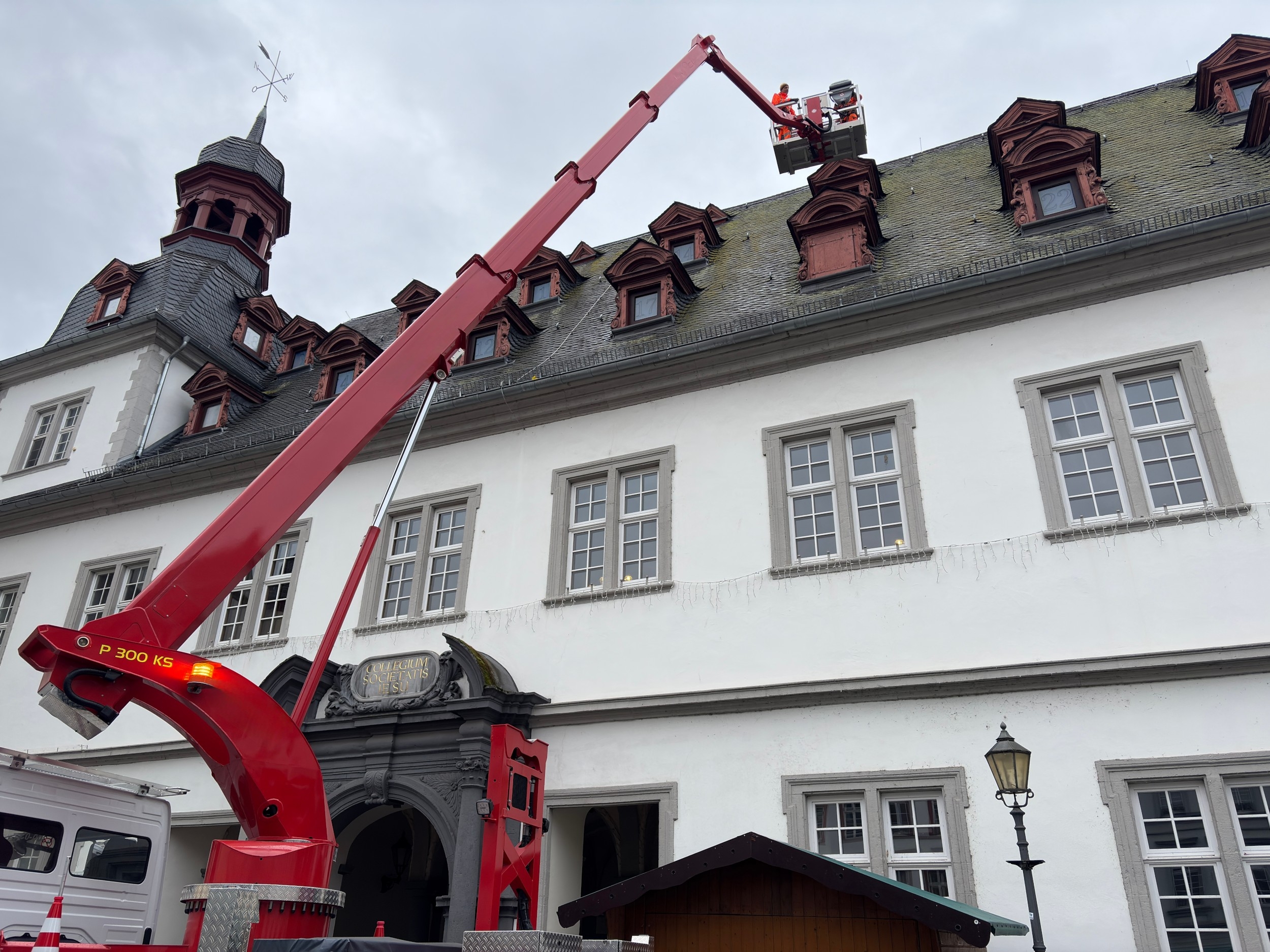 Mit einem Hubsteiger sind Arbeiter damit beschäftigt, Fensterläden von Dachgauben abzunehmen.