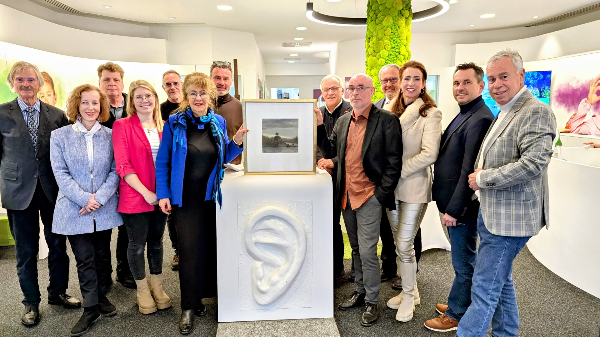 Gruppenfoto bei dem ein Tresen in der Mitte steht auf dem ein Bild von zwei Personen festgehalten wird.