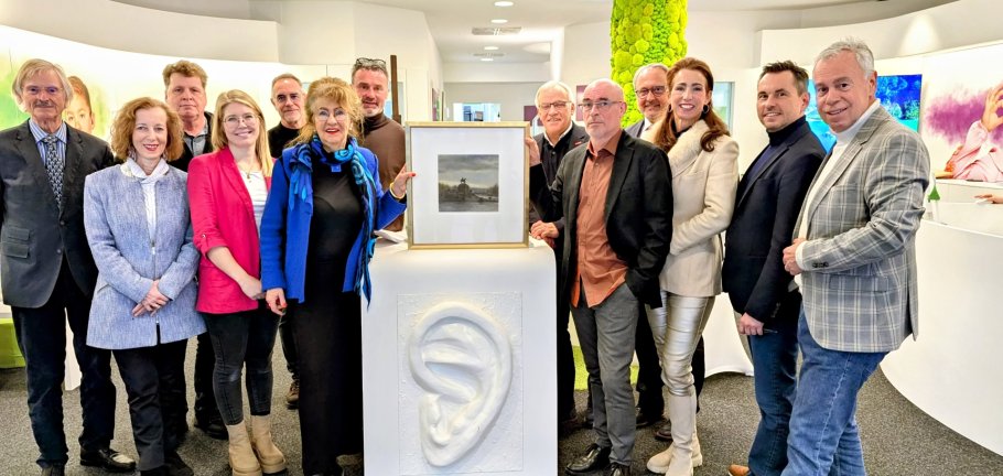 Gruppenfoto bei dem ein Tresen in der Mitte steht auf dem ein Bild von zwei Personen festgehalten wird.