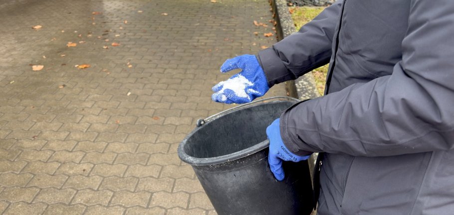 Ein Mensch mit Streumitteleimer.