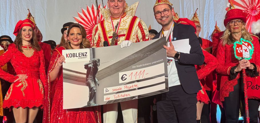 Zwei Männer und eine Frau in Karnevalskostümen halten einen Spendenscheck in Höhe von 1111 Euro in ihren Händen.