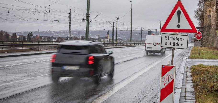 Ein Auto fährt auf einer Straße an einem Schild vorbei. Auf dem Schild steht Straßenschäden als Aufschrift.