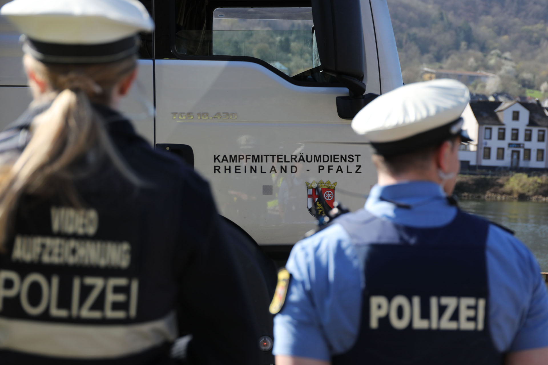 Zwei Polizisten stehen vor einer LKW-Tür mit der Aufschrift Kampfmittelräumdienst Rheinland-Pfalz.