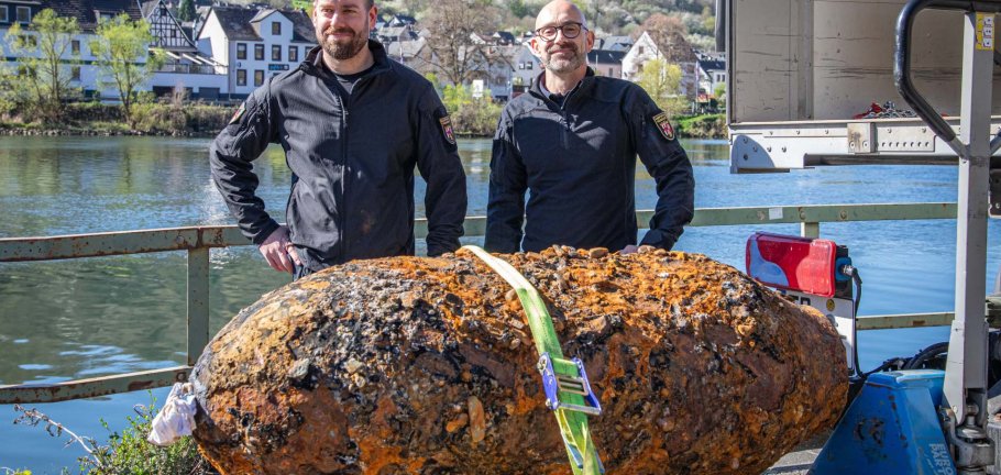 Zwei Männer stehen hinter einer entschärften Bombe.