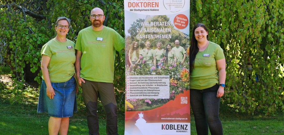 Drei Personen stehen vor einem Werbebanner. Drei Personen stehen vor einem Werbebanner.