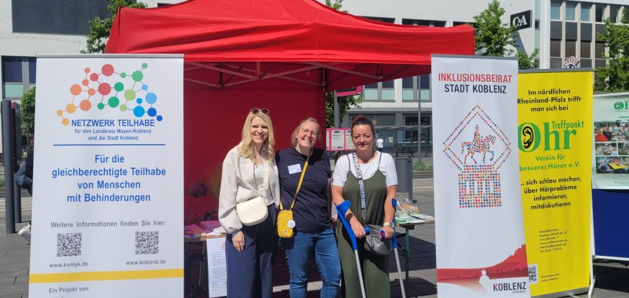 Drei Frauen stehen vor einem Informationsstand. Drei Frauen stehen vor einem Informationsstand.