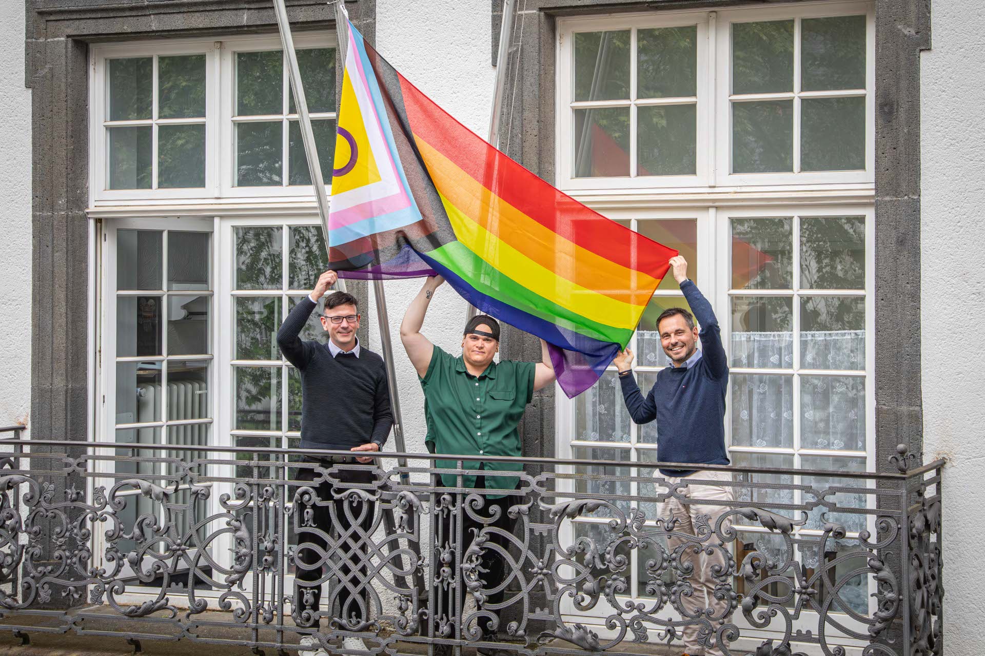 Drei Personen stehen auf einem Balkon und halten eine Flagge in ihren Händen.